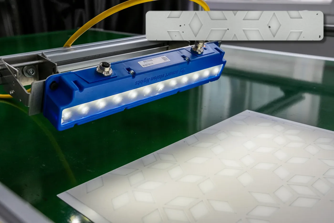 Industrial inspection head and lighting for visual quality control Inspection head and blue LED lighting mounted above a patterned material sample in an industrial vision setup.